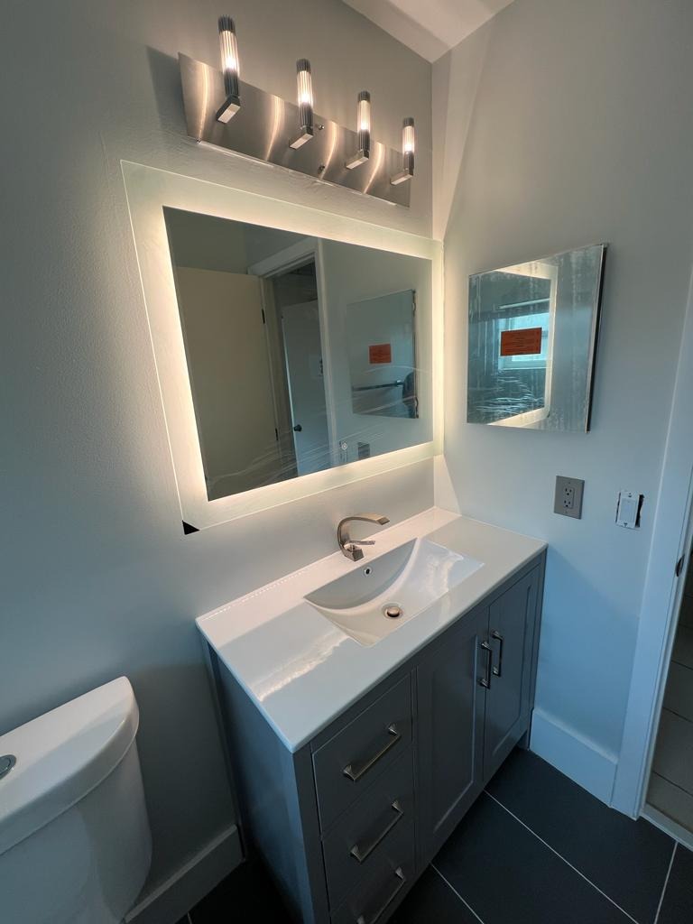 Remodeled bathroom with backlit LED mirror, grey vanity and dark tile floor - Handyman Group SFL