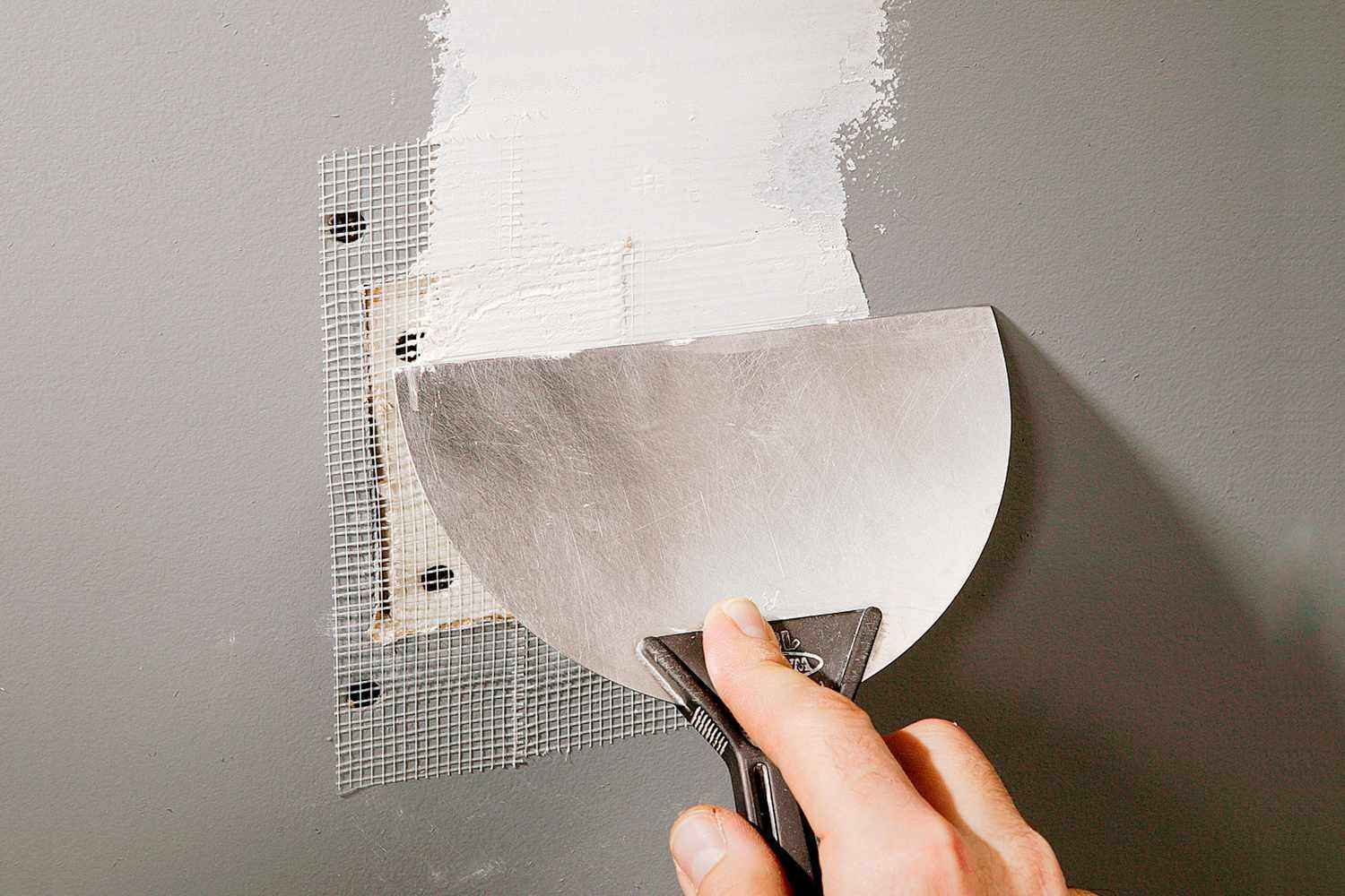 Taping knife spreading compound over a mesh drywall patch - Handyman Group SFL